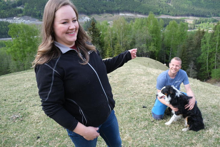 Irene står i front og peker utover dalen, i bakgrunn sitter Stig Ola på huk sammen med gjeterhunden Pei.
